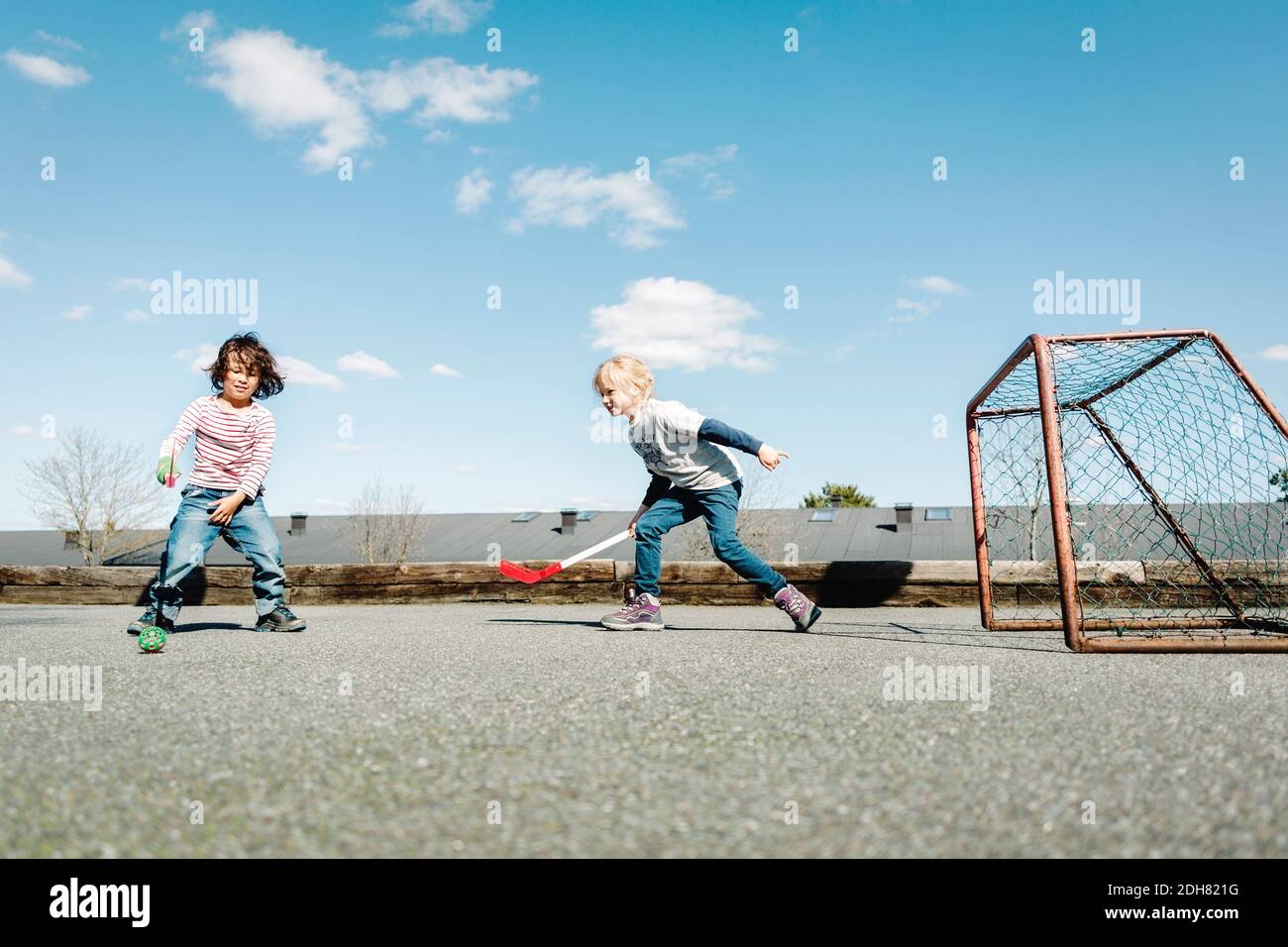 Kinder spielen Hockey auf dem Hof gegen blauen Himmel Stockfoto Kinder spielen Hockey auf dem Hof gegen blauen Himmel Stockfoto