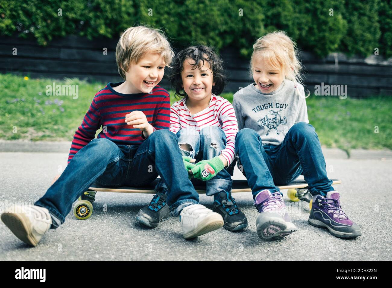 Spielerische Freunde sitzen auf dem Skateboard auf dem Hof Stockfoto