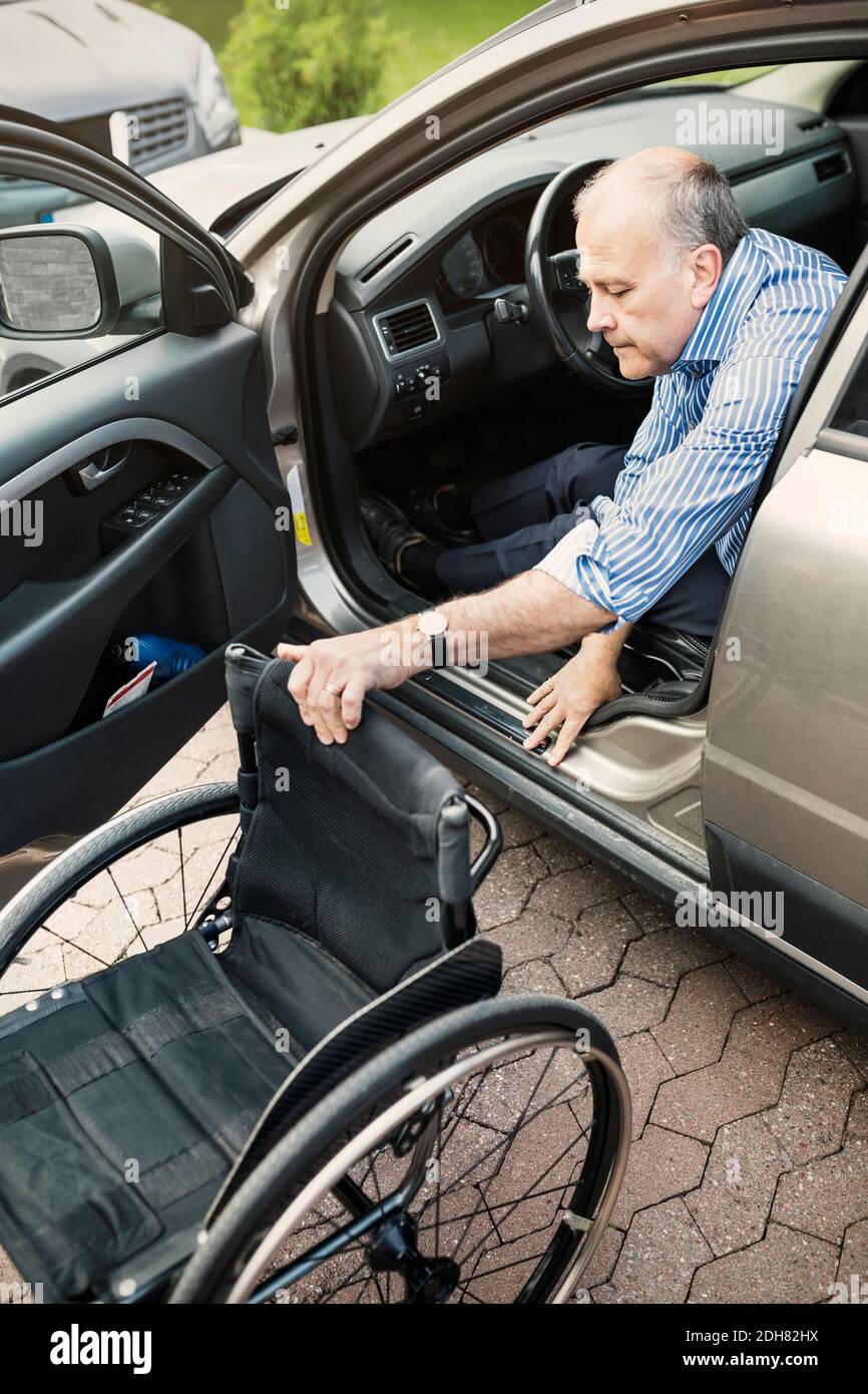 Behinderter Mann, der den Rollstuhl zieht, während er das Auto auf der Straße aussteigt Stockfoto