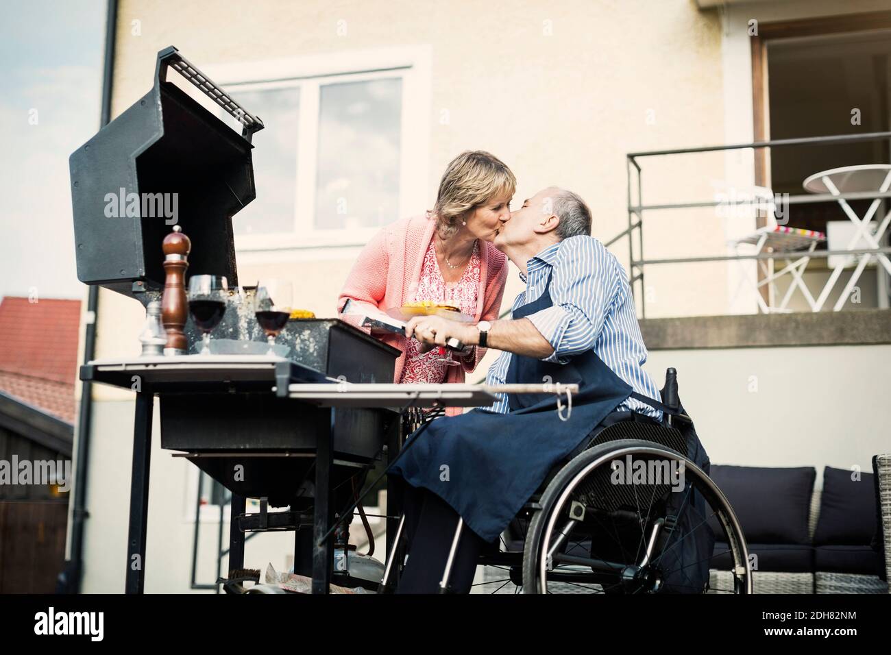 Behinderter Mann im Rollstuhl küsst Frau beim Grillen auf dem Hof Stockfoto