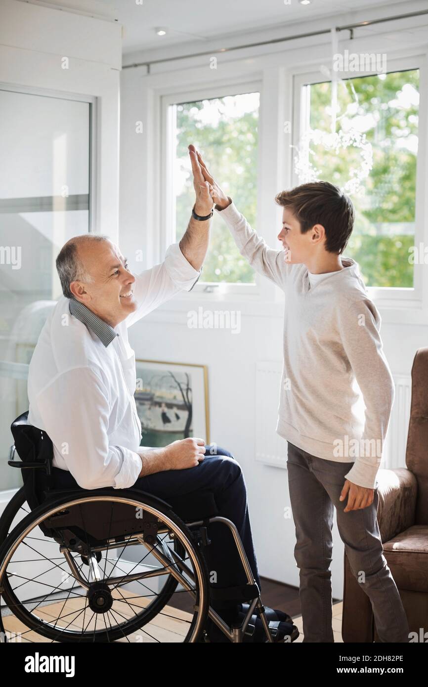 Behinderter Mann im Rollstuhl, der dem Sohn zu Hause fünf hoch gibt Stockfoto