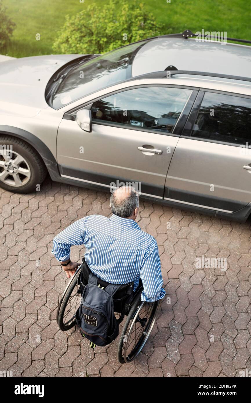 High-Angle-Ansicht des reifen Mannes im Rollstuhl in Richtung bewegen Auto auf der Straße Stockfoto