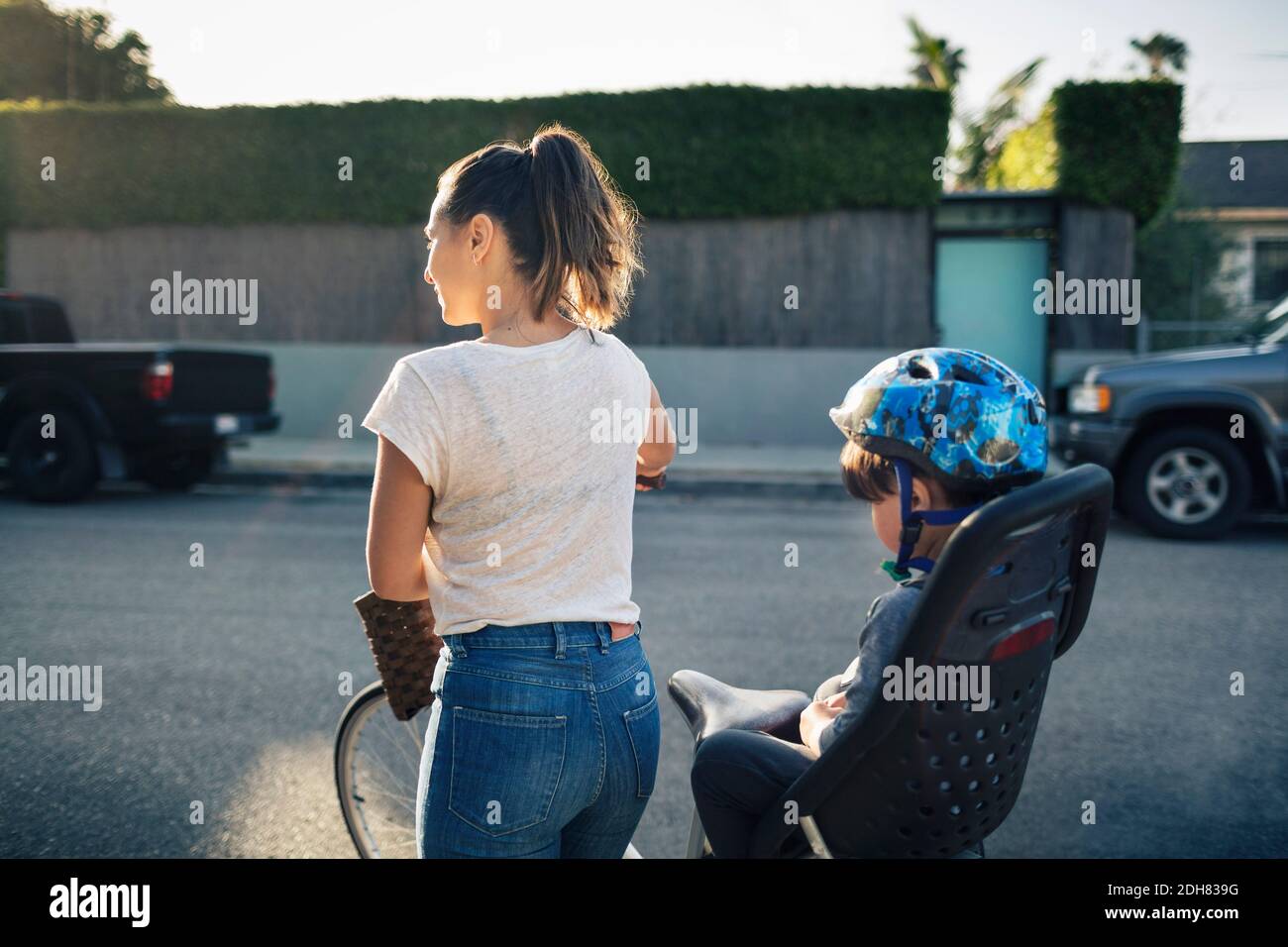Rückansicht einer Frau, die Fahrrad hält und auf dem Sohn sitzt Rücksitz im Freien Stockfoto