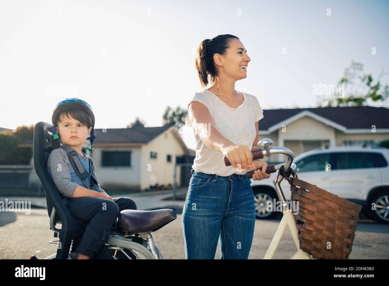 Glückliche Frau schaut weg, während Sohn auf dem Fahrrad im Freien sitzt Stockfoto