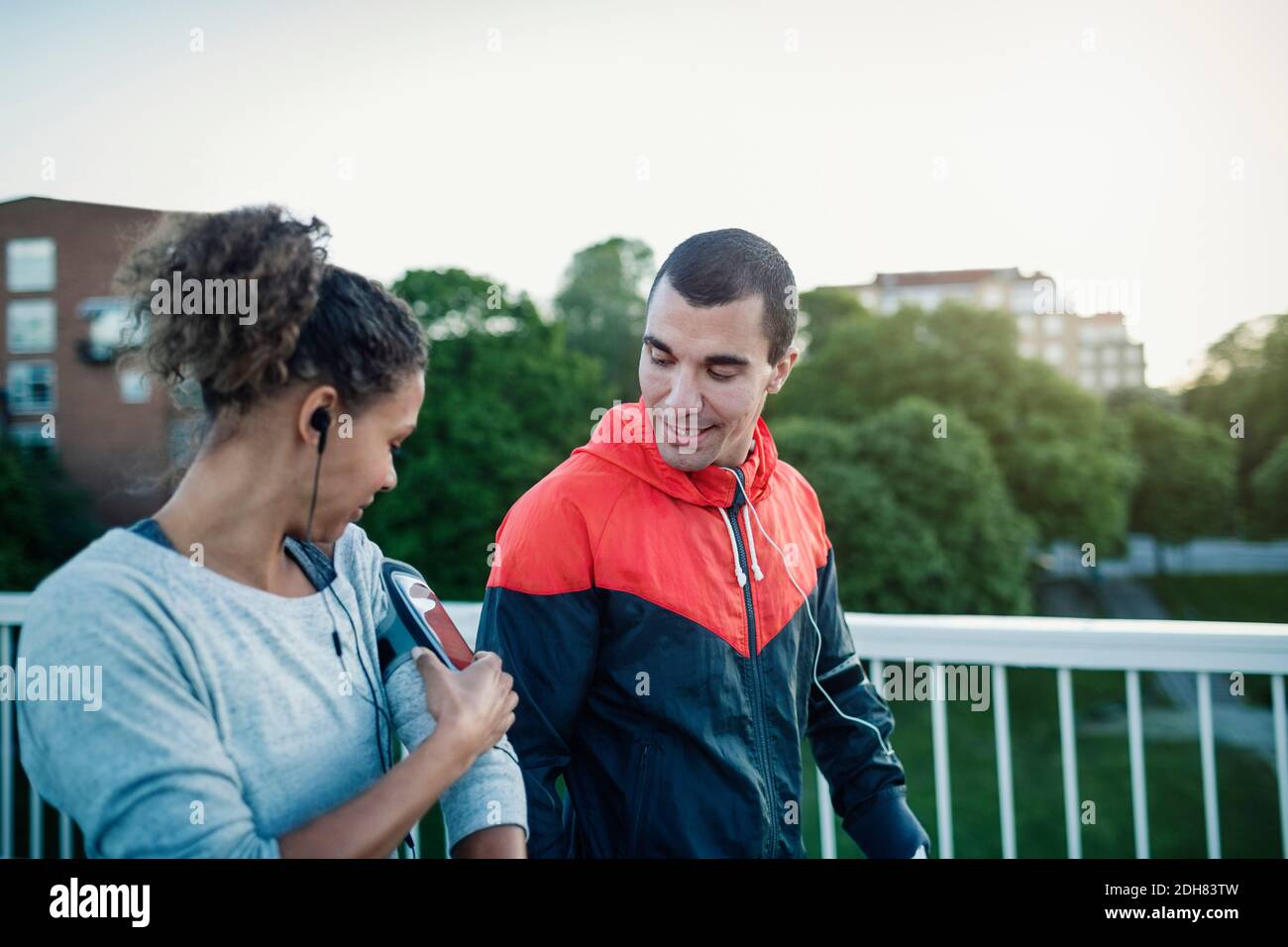 Mann, der Frau beim Gehen mit dem Armband eines Smartphones ansieht Auf dem Bürgersteig Stockfoto