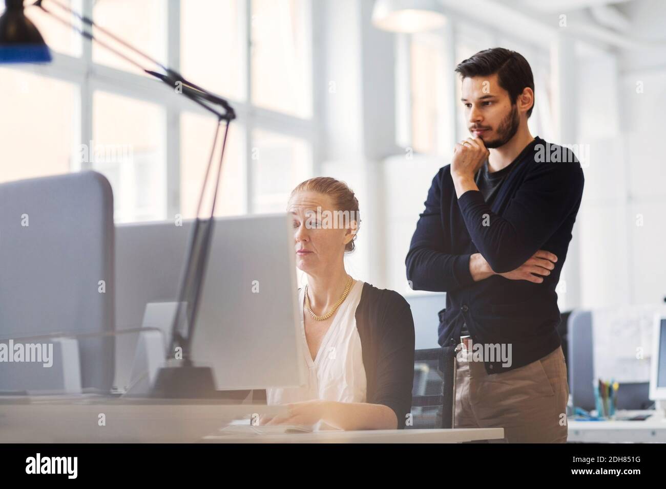 Mittelerwachsener Geschäftsmann, der eine Kollegin mit dem Computer ansieht Büro Stockfoto