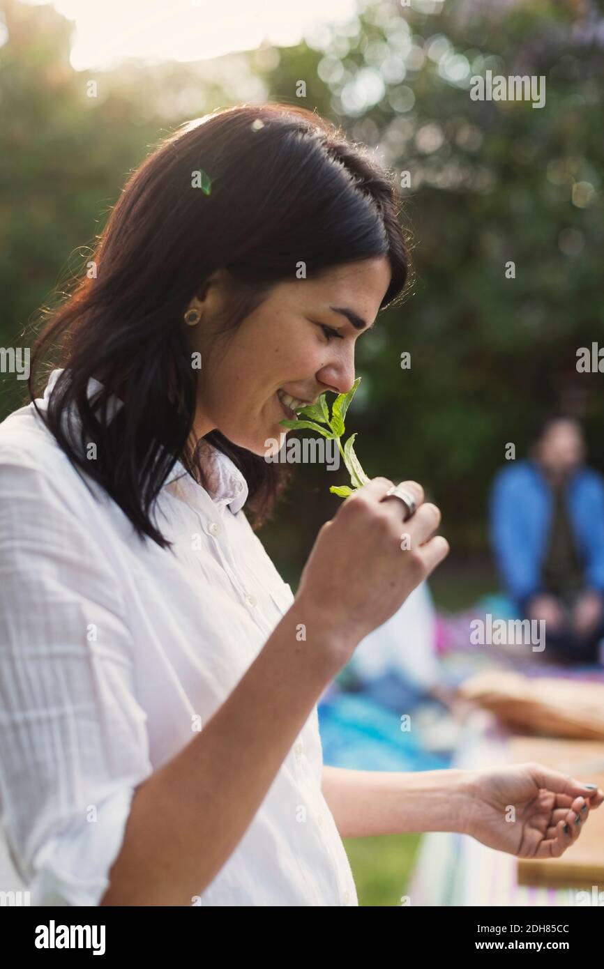 Seitenansicht einer glücklichen jungen Frau, die beim Zubereiten Kraut riecht Essen im Hinterhof Stockfoto