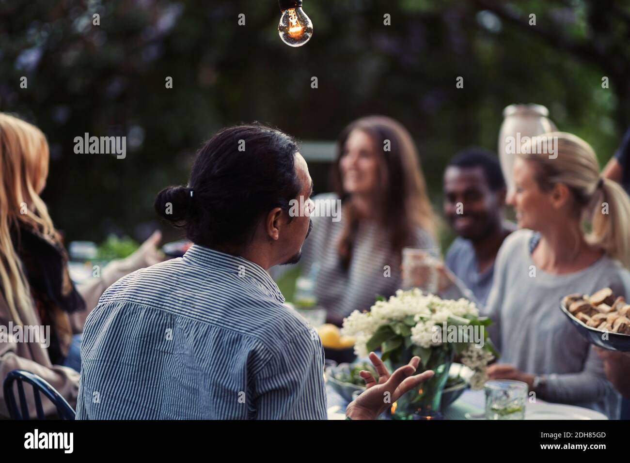 Rückansicht des Mannes, der mit Freunden am Esstisch sitzt Bei der Dinnerparty im Freien Stockfoto