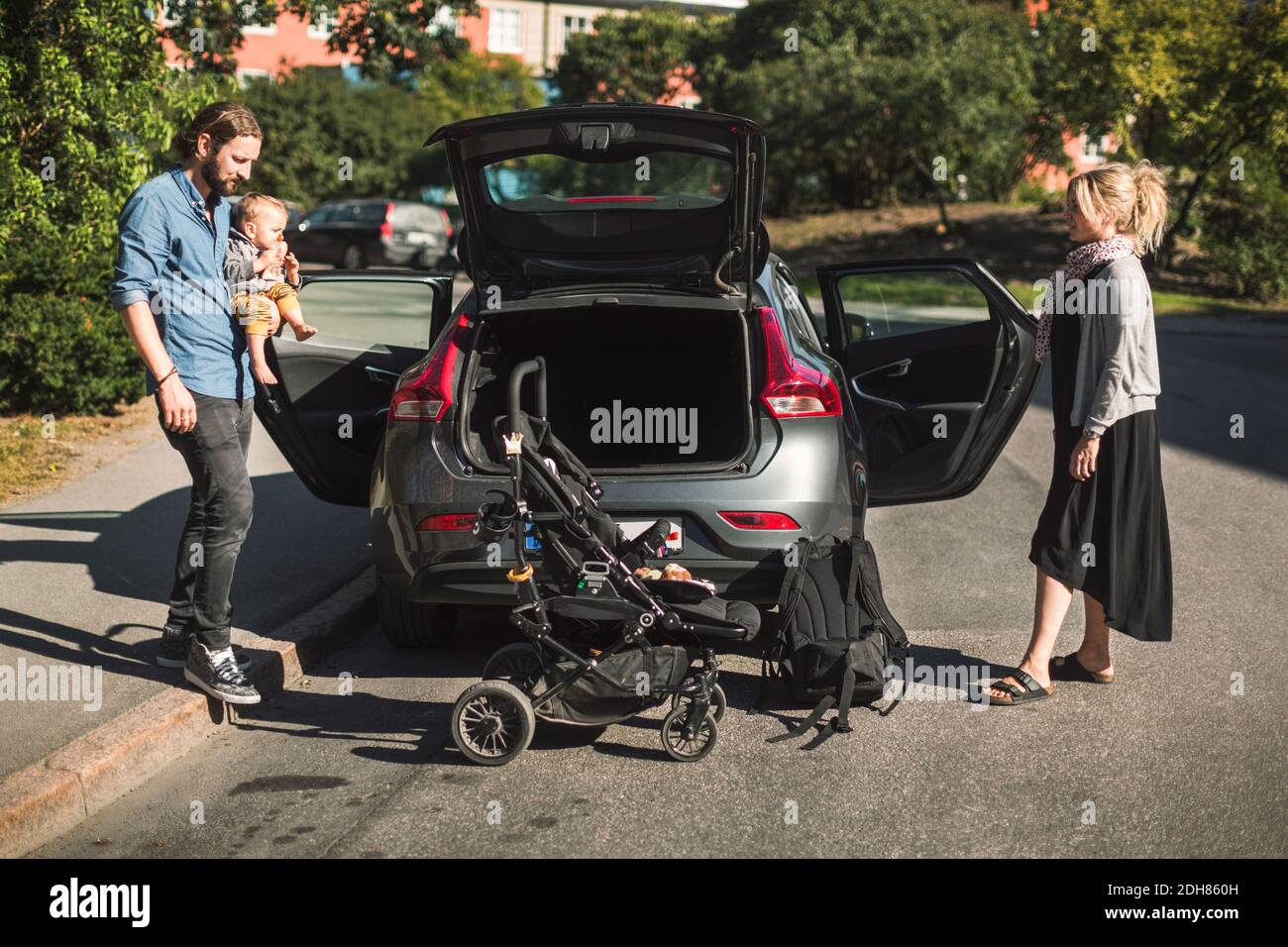 Volle Länge der mittleren erwachsenen Eltern mit Sohn und Baby Kinderwagen in der Nähe des Autos auf der Straße Stockfoto