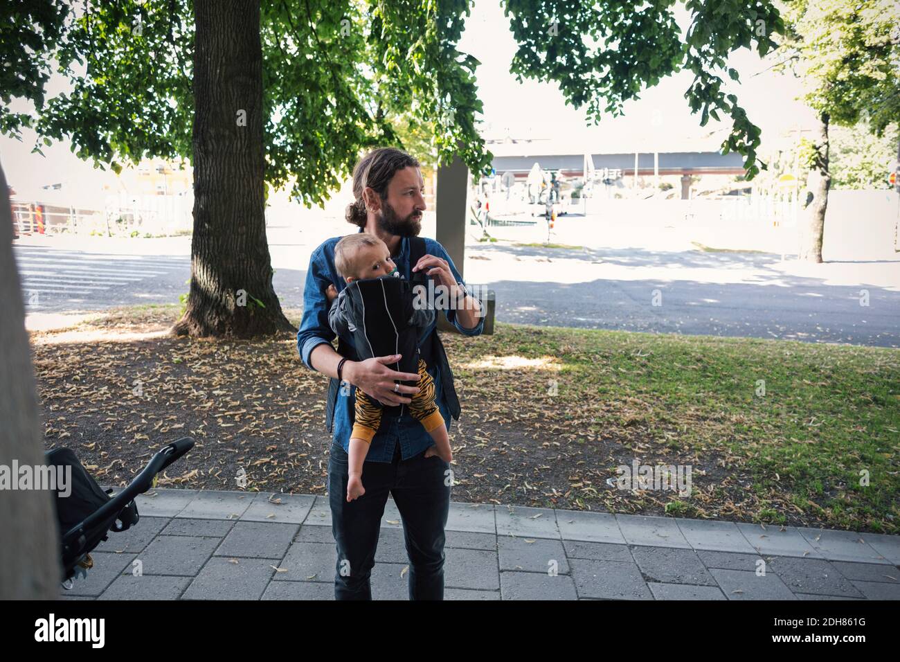 Mittlerer Erwachsener Vater trägt Baby in Träger auf Bürgersteig Stockfoto
