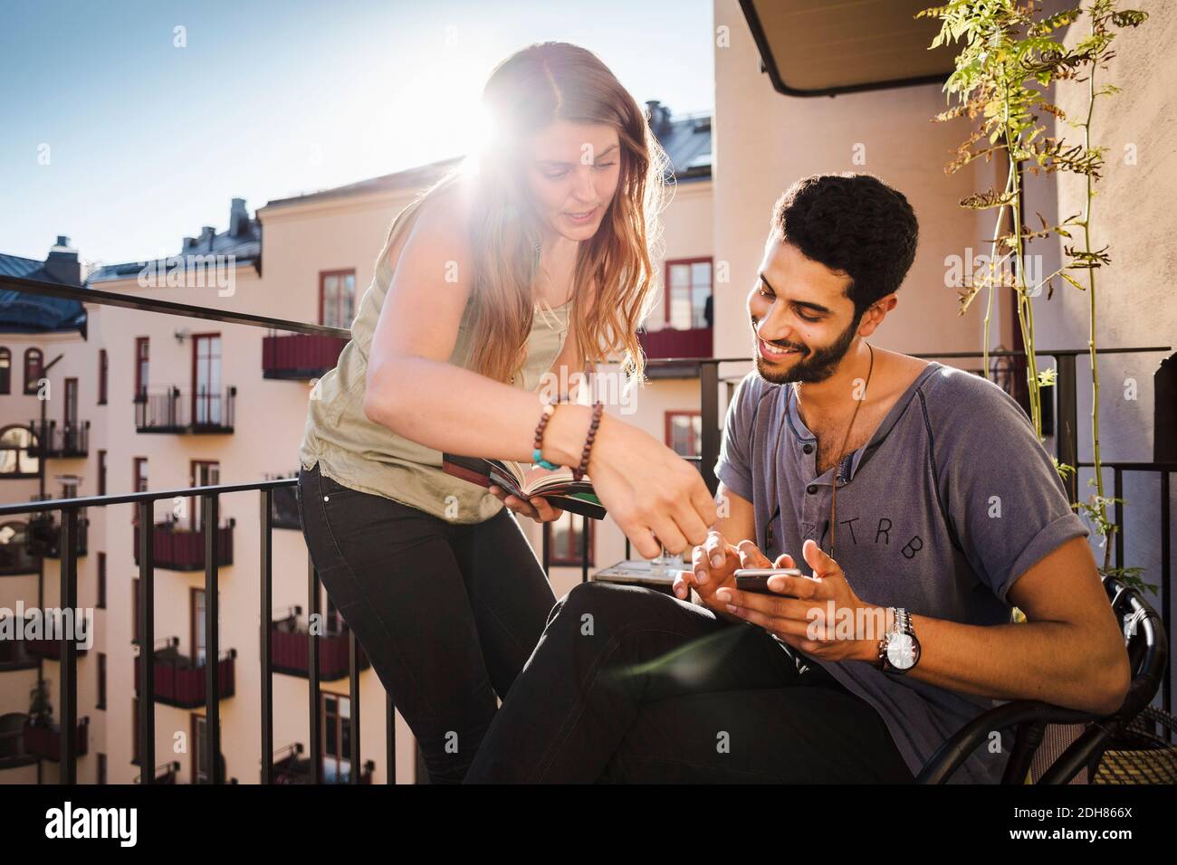 Glückliches Paar, das Smartphone benutzte, während es den Reiseführer auf dem Balkon las Stockfoto