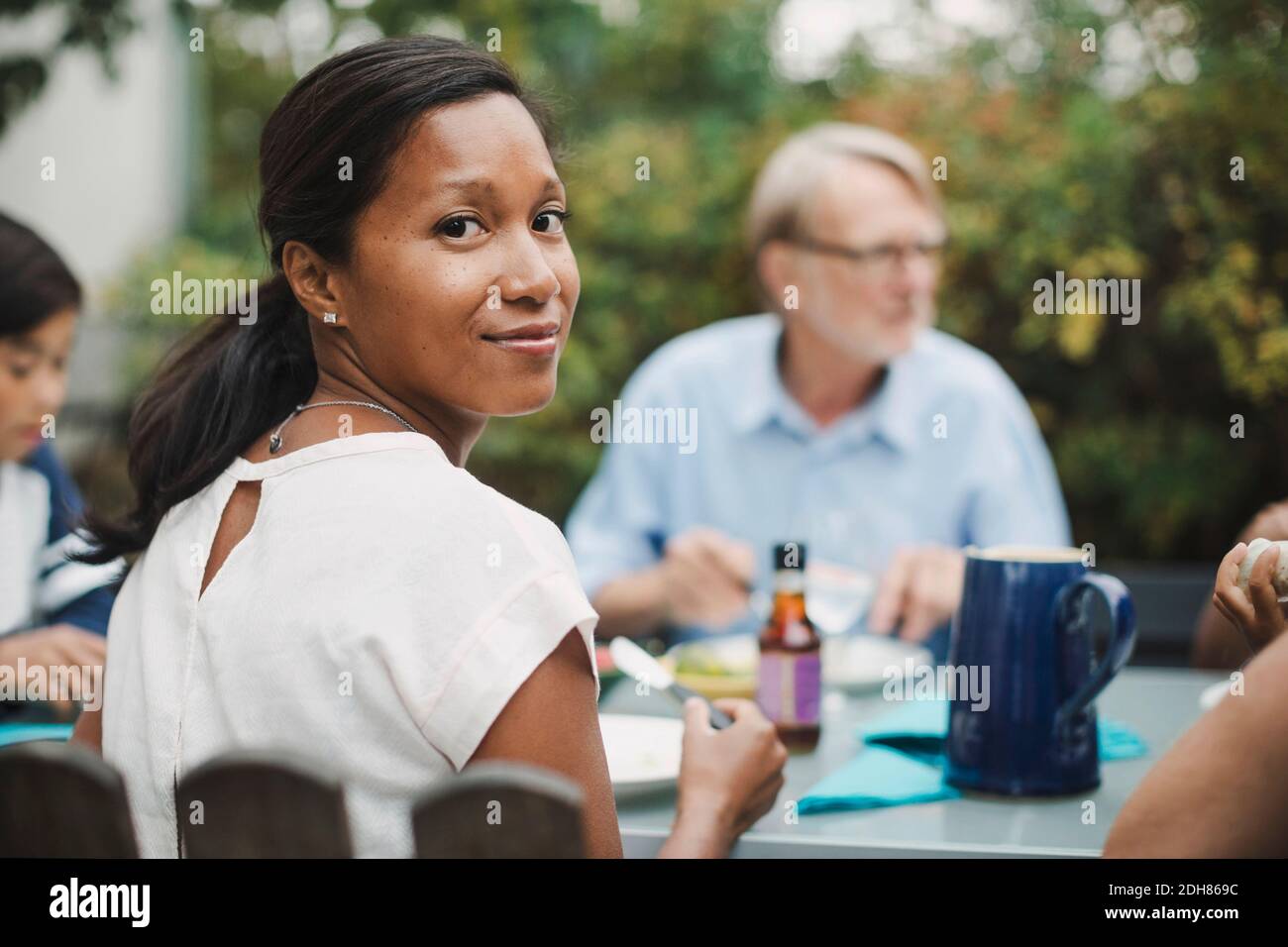 Rückansicht Porträt der Frau mit Essen mit Familie an Außentisch Stockfoto