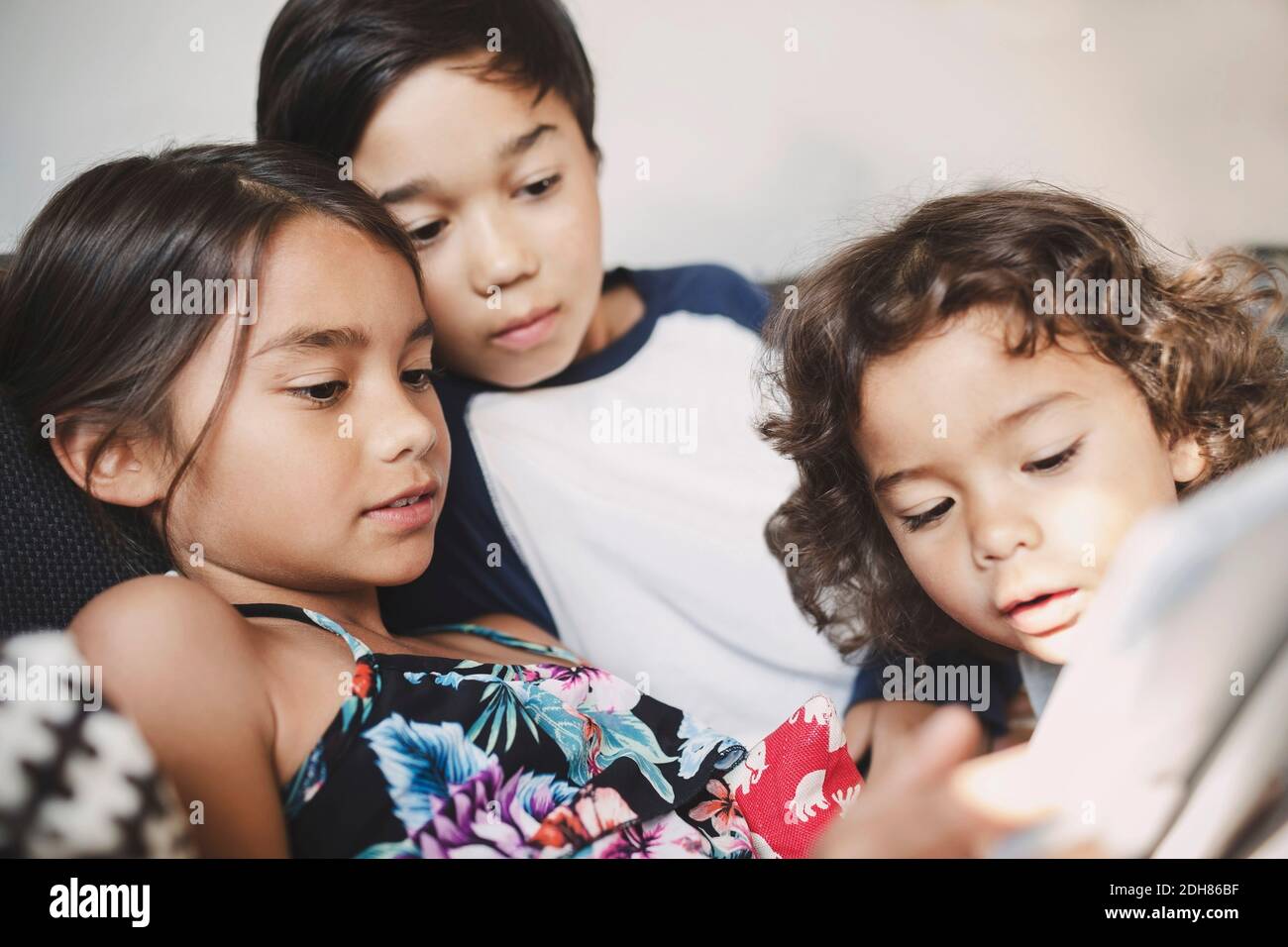 Brüder und Schwester, die zu Hause ein digitales Tablet auf dem Sofa benutzen Stockfoto