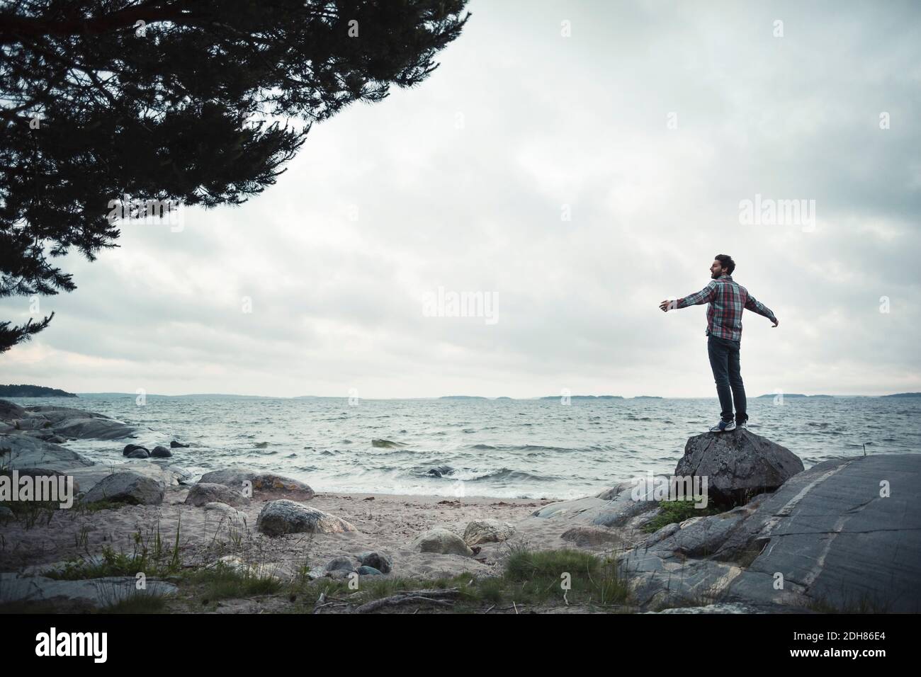 Rückansicht des wonderlust-Mannes, der mit ausgestreckten Armen steht Rock by Sea Stockfoto