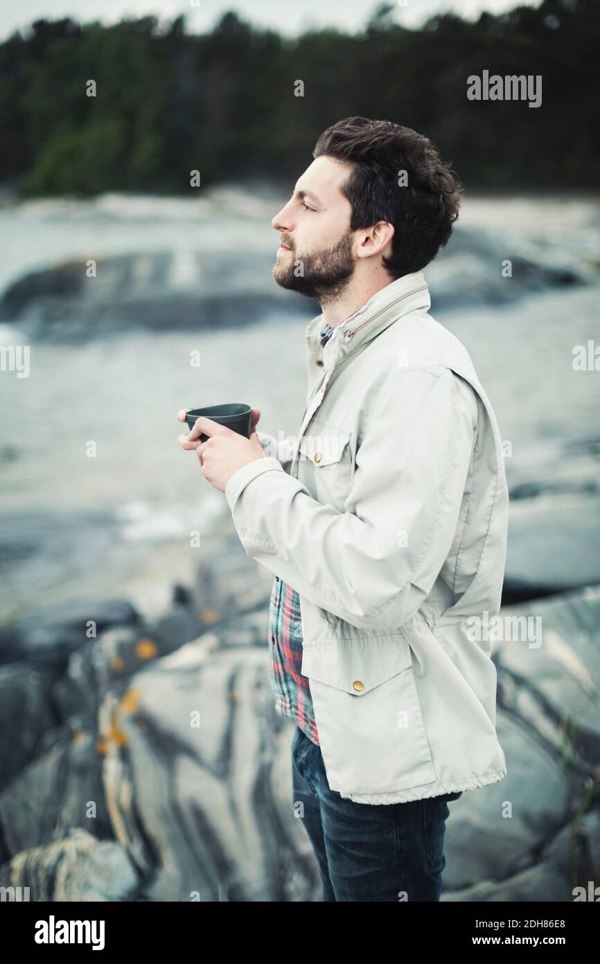Seitenansicht des wonderlust-Mannes, der im Stehen einen Kaffeebecher hält Auf Felsen Stockfoto