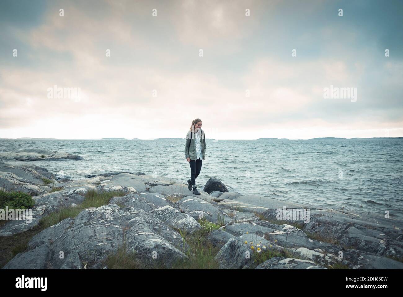 Wonderlust Frau auf Felsen am Meer gegen bewölkten Himmel zu Fuß Stockfoto