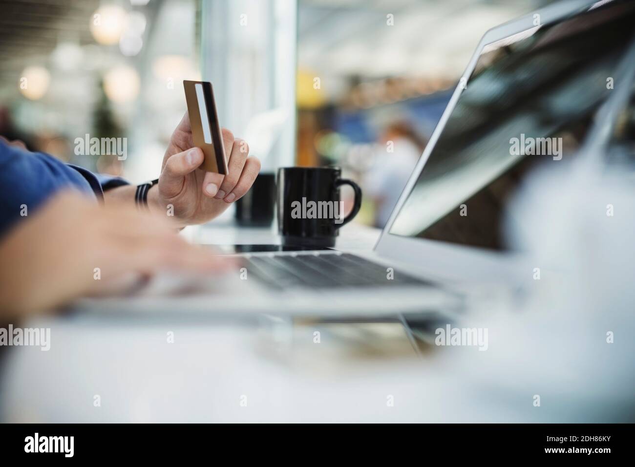 Zugeschnittenes Bild von Geschäftsmann mit Kreditkarte und Laptop an flughafenlobby Stockfoto