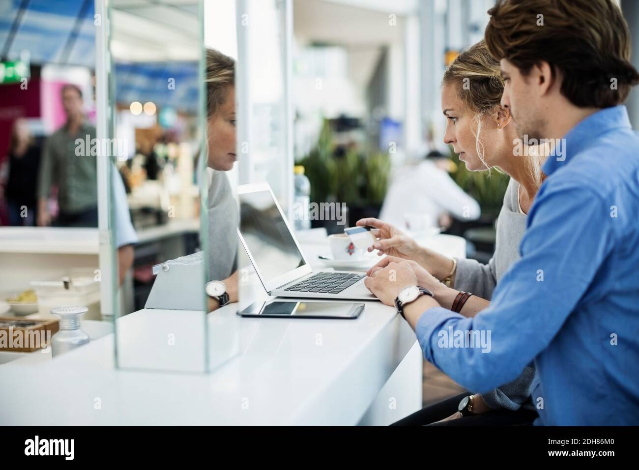 Seitenansicht von Geschäftsleuten mit Kreditkarte und Laptop In der Flughafenlobby Stockfoto