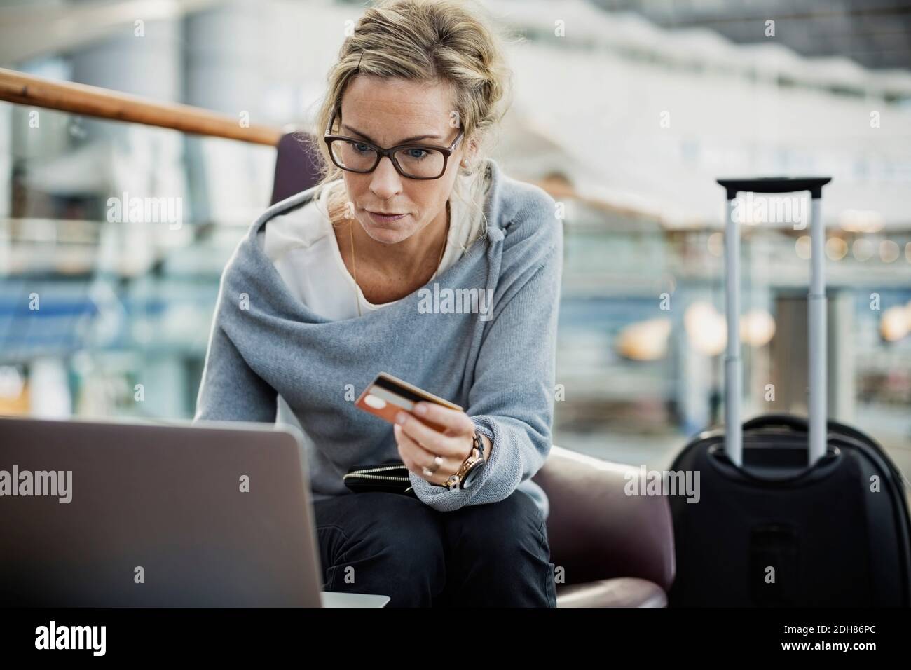 Geschäftsfrau mit Kreditkarte und Laptop in der Flughafenlobby Stockfoto