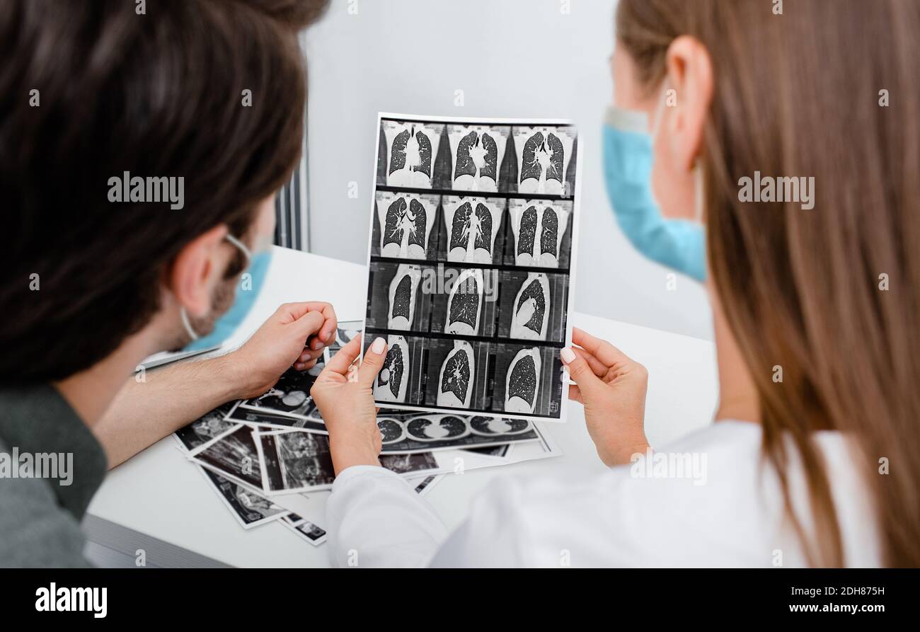 Der Pneumologe trägt eine Schutzmaske und zeigt dem Patienten einen CT-Scan seiner Lunge. Lungenentzündung, Coronavirus, Lungenerkrankung Stockfoto