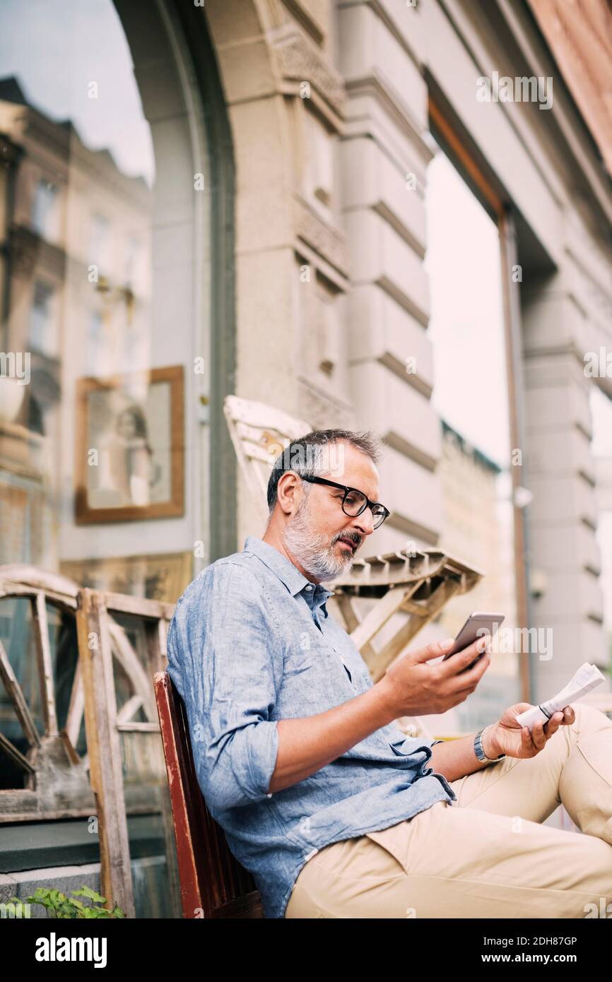 Mann, der Handy benutzt, während er vor dem Geschäft sitzt Stockfoto