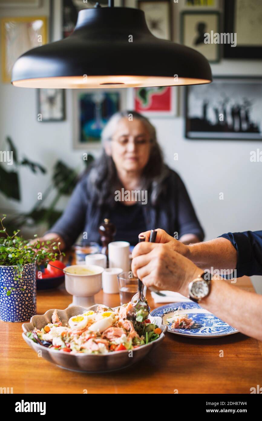 Zugeschnittenes Bild eines Mannes, der Salat am Esstisch serviert Stockfoto