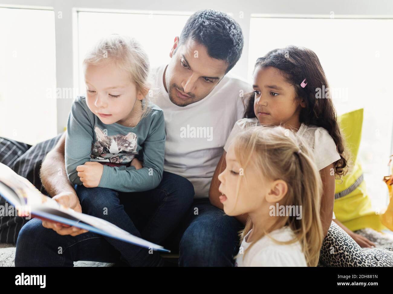 Männlicher Lehrer und Mädchen lesen Geschichte Buch in der Tagesbetreuung Zentrieren Stockfoto