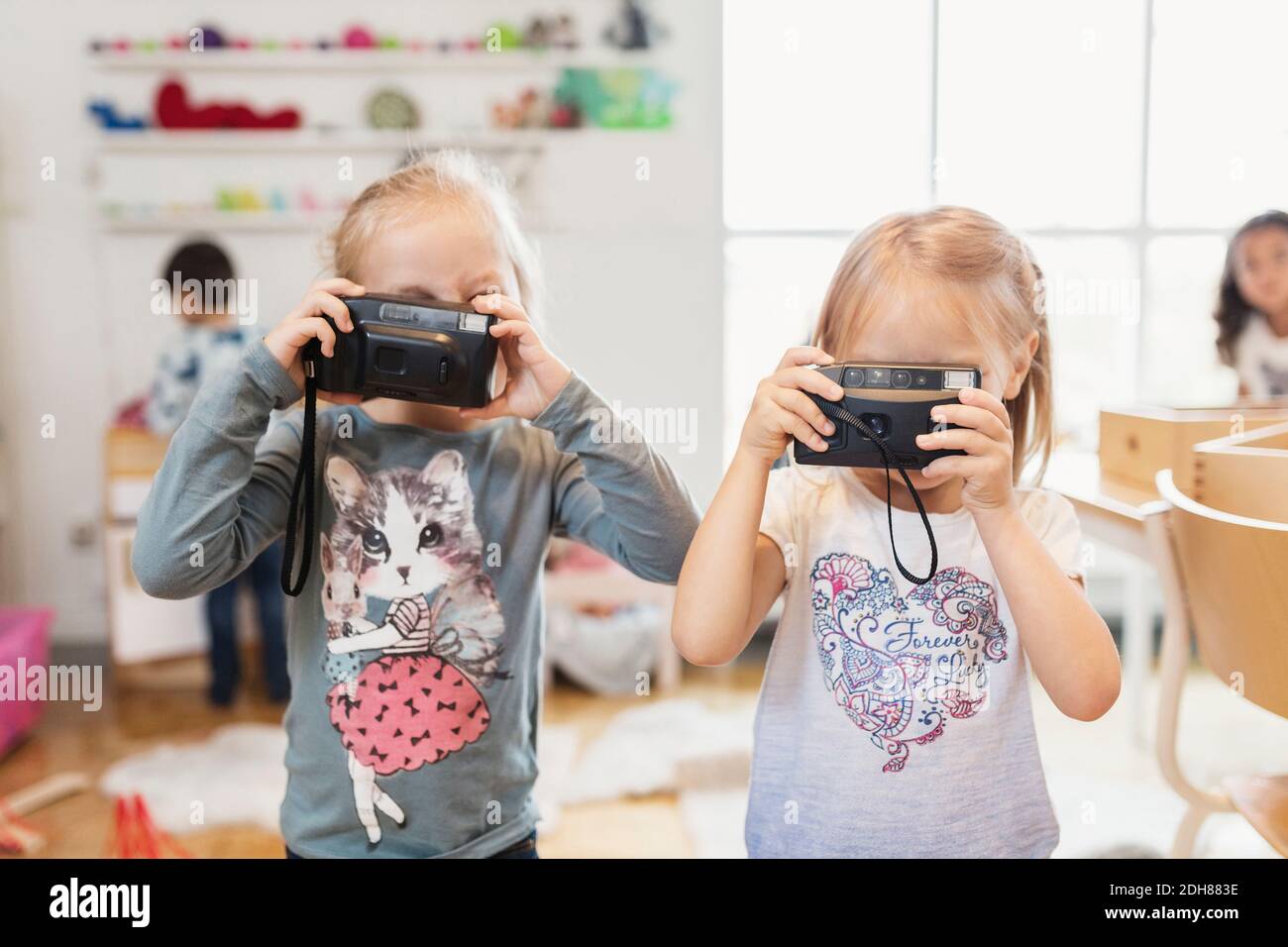 Kleine Mädchen halten Spielzeugkameras im Klassenzimmer Stockfoto
