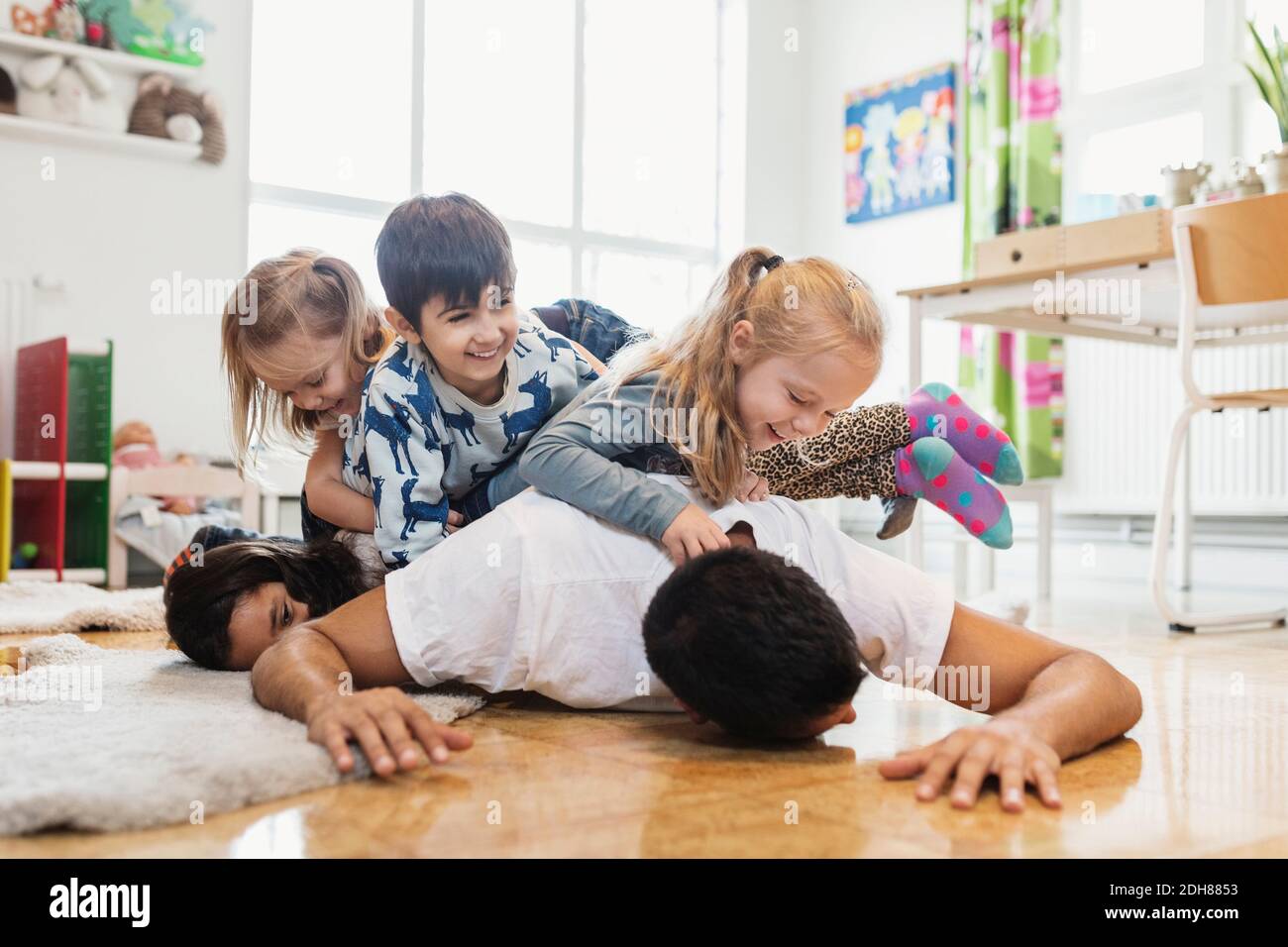 Glückliche Kinder, die auf dem Lehrer im Kindergarten liegen Stockfoto