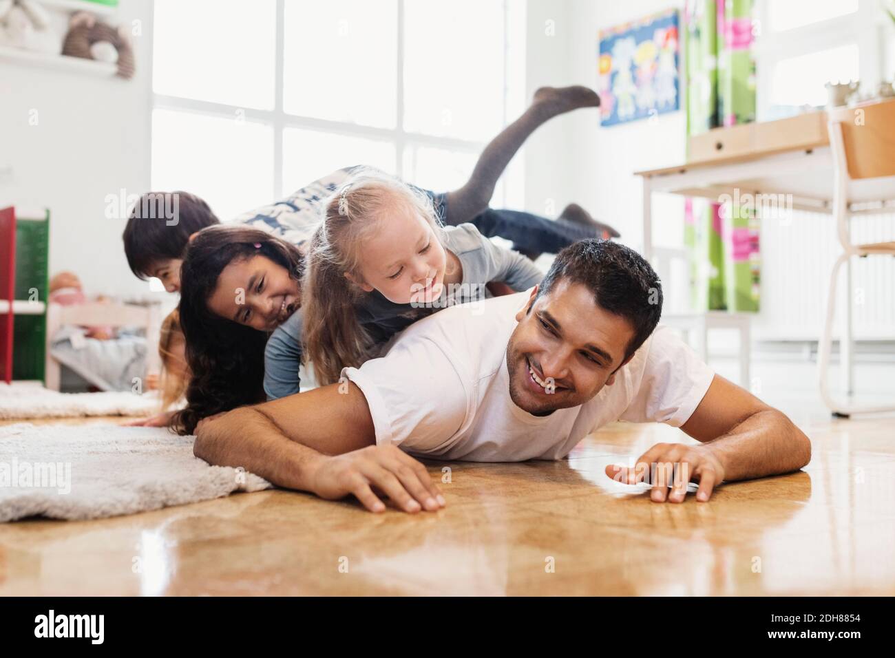 Glückliche Kinder liegen auf dem männlichen Lehrer im Kindergarten Stockfoto