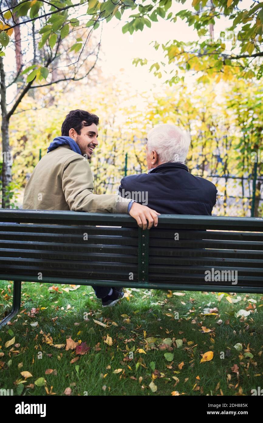 Rückansicht des Hausmeisters, der während des Sitzens einen älteren Mann ansah Auf der Bank im Park Stockfoto
