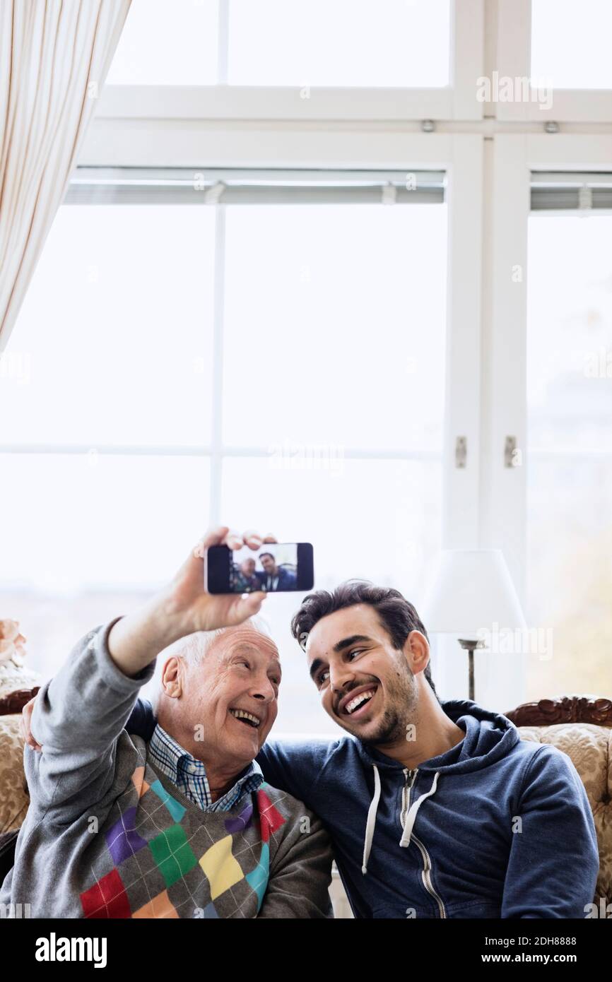 Glücklicher Mann nimmt Selfie mit jungen Hausmeister im Pflegeheim Stockfoto