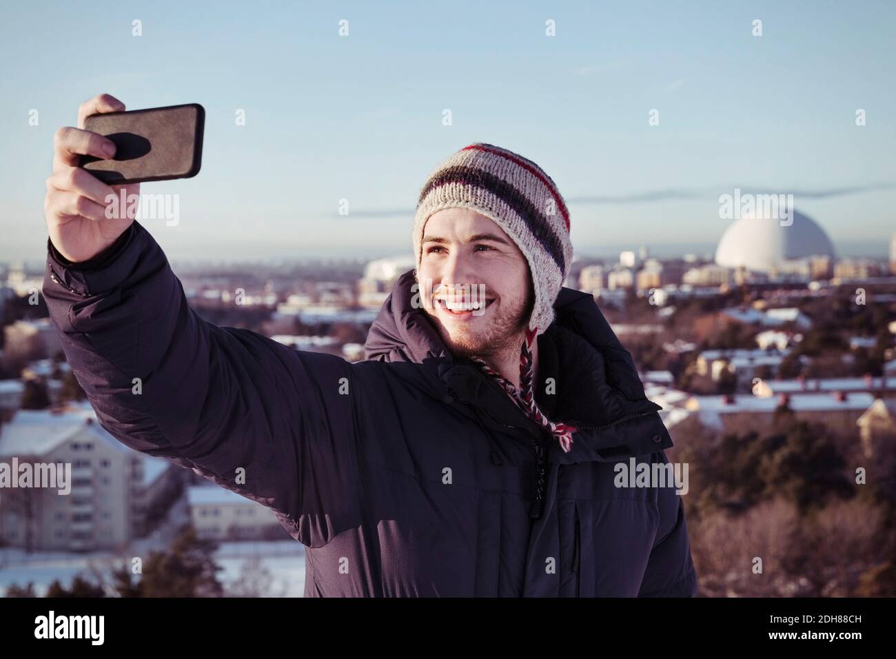 Lächelnder junger Mann, der im Winter Selfie über das Smartphone klickt Stockfoto