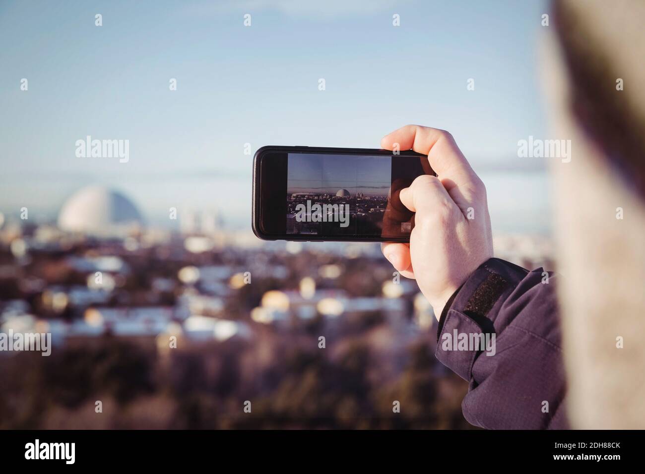 Zugeschnittenes Bild des Menschen beim Fotografieren der Stadtlandschaft über das Mobiltelefon während Winter Stockfoto