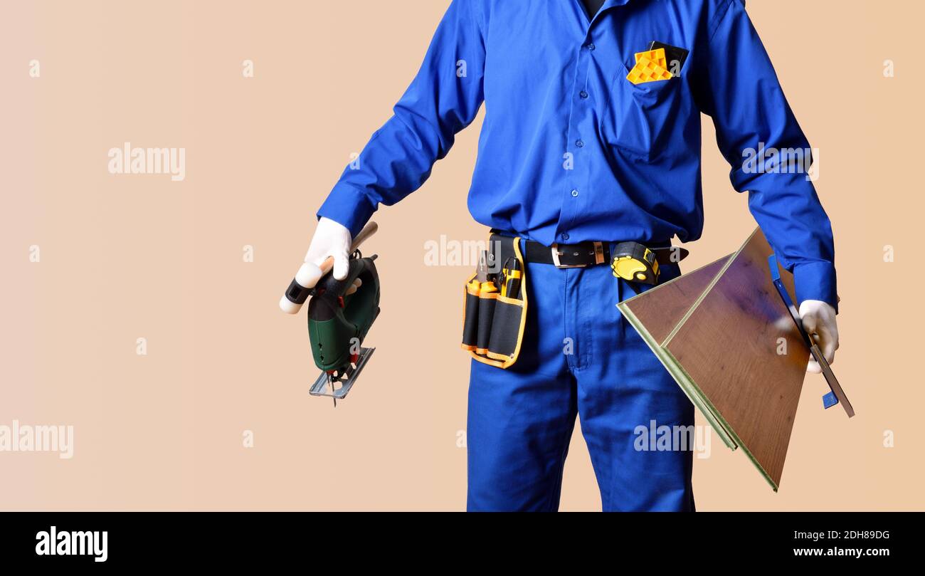 Hintergrund Detail des Körpers eines Parkett-Installateur in Overalls gekleidet und mit Werkzeugen und Parkettbohlen versehen. Horizontale Zusammensetzung. Stockfoto