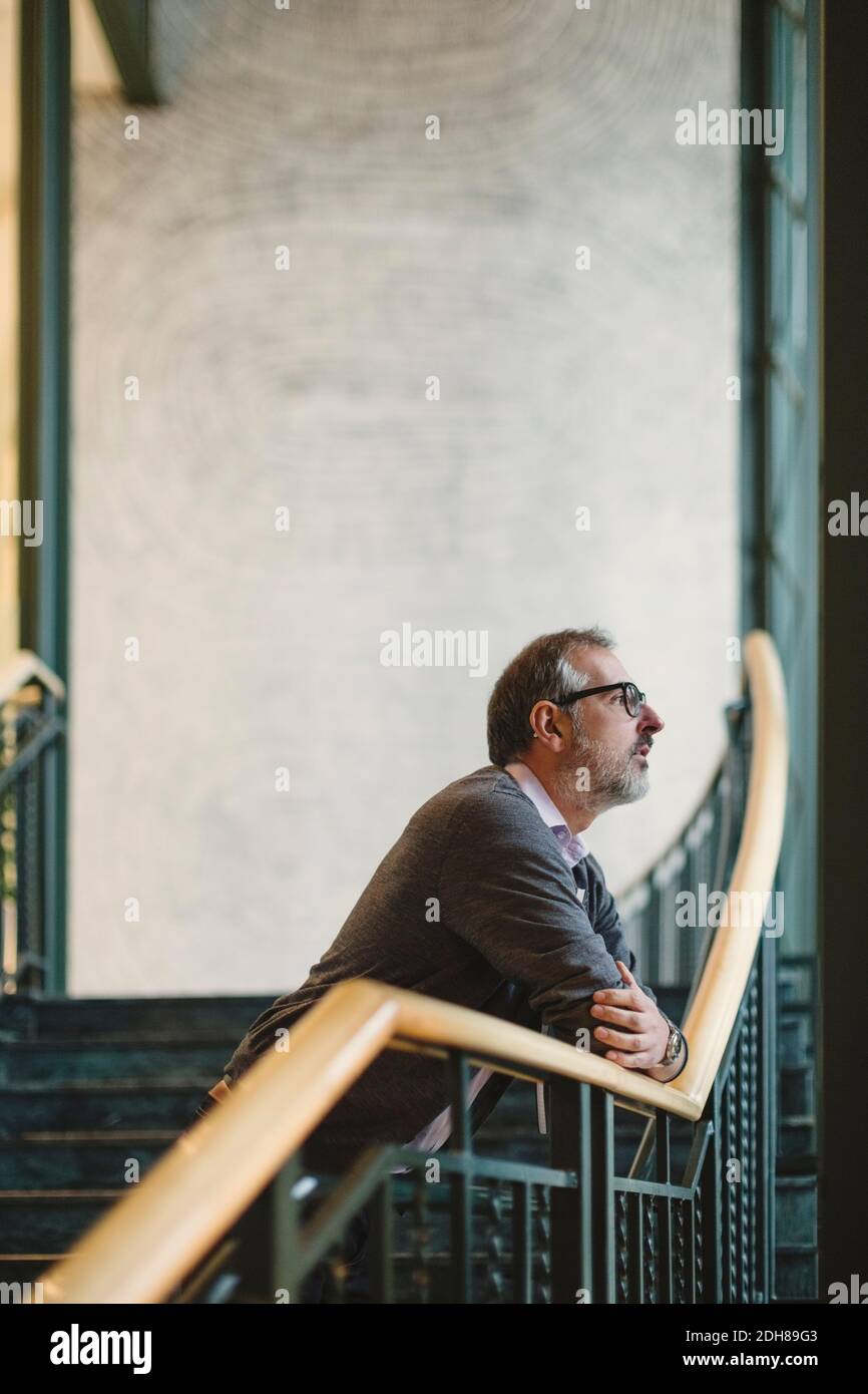 Nachdenklicher Geschäftsmann, der sich im kreativen Büro am Treppenaufgang auf das Geländer stützt Stockfoto