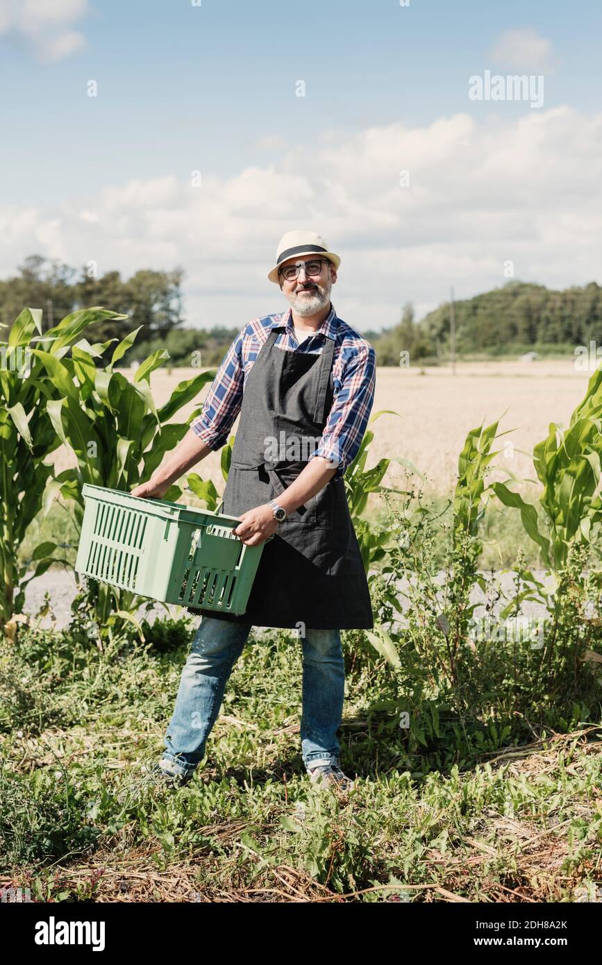 Porträt eines lächelnden reifen Gärtners, der Kiste hält und an dem er steht Bauernhof Stockfoto