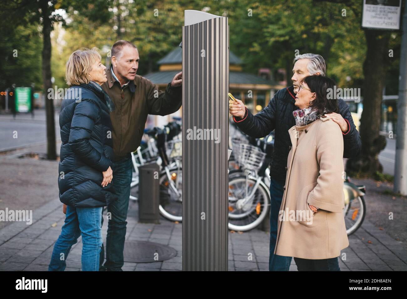 Zwei ältere Paare, die die Zahlung an der Fahrradverleih-Station Stockfoto