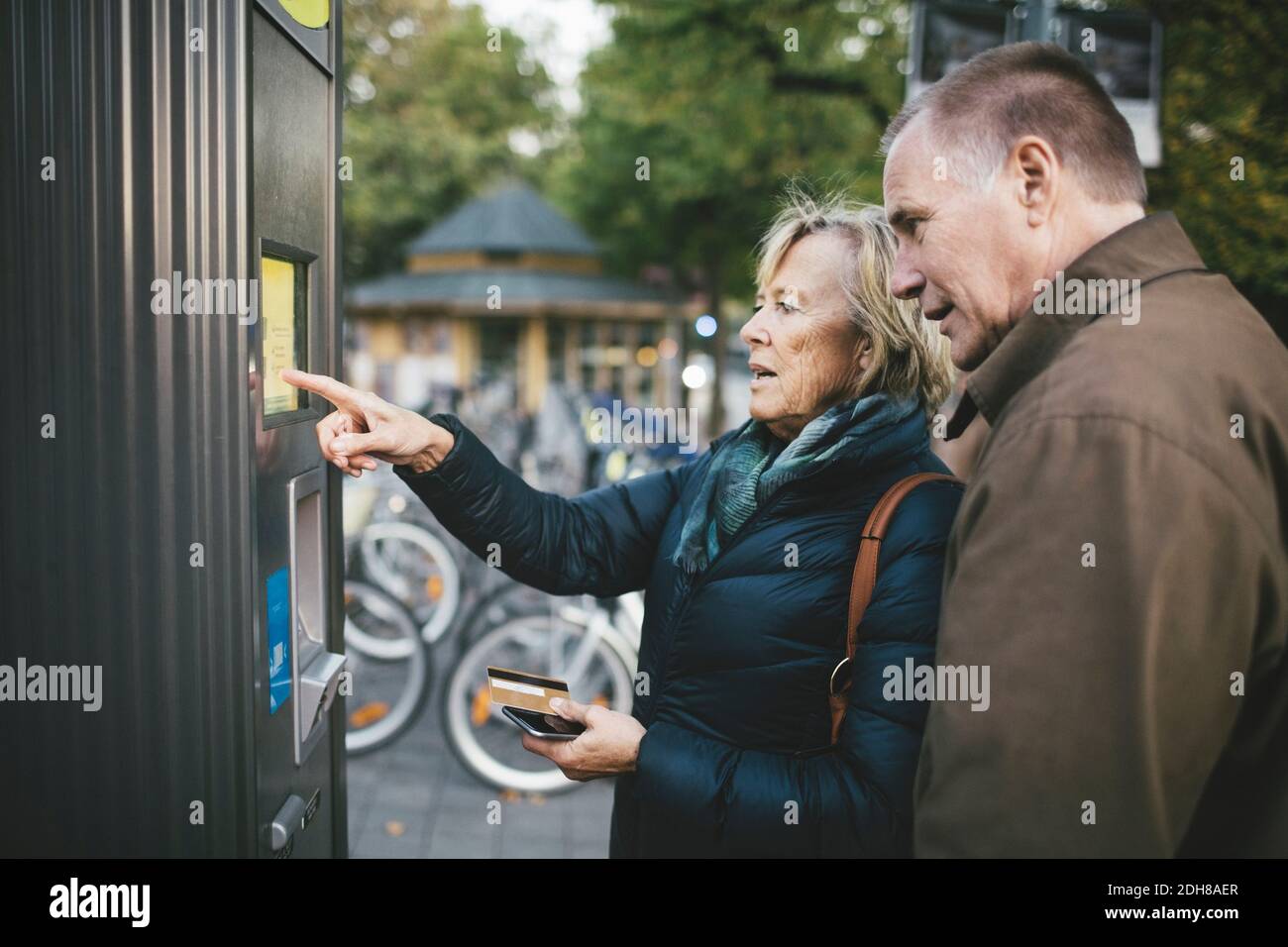 Älterer Mann mit Frau, die die Zahlung per Kreditkarte bei Fahrradverleih Stockfoto