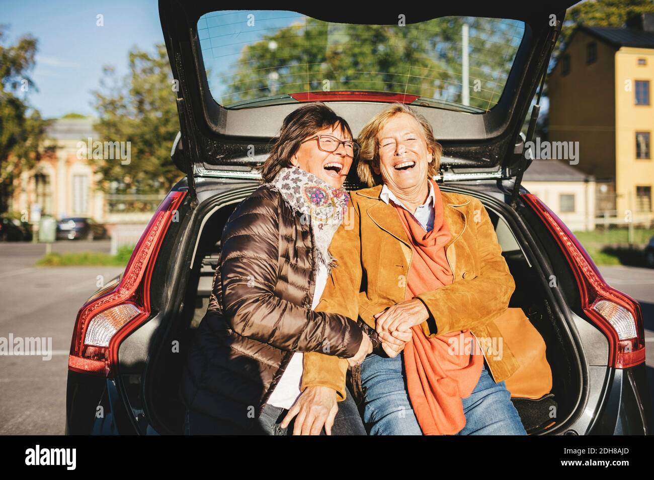 Glückliche ältere Frau, die im geöffneten Kofferraum sitzt Stockfoto