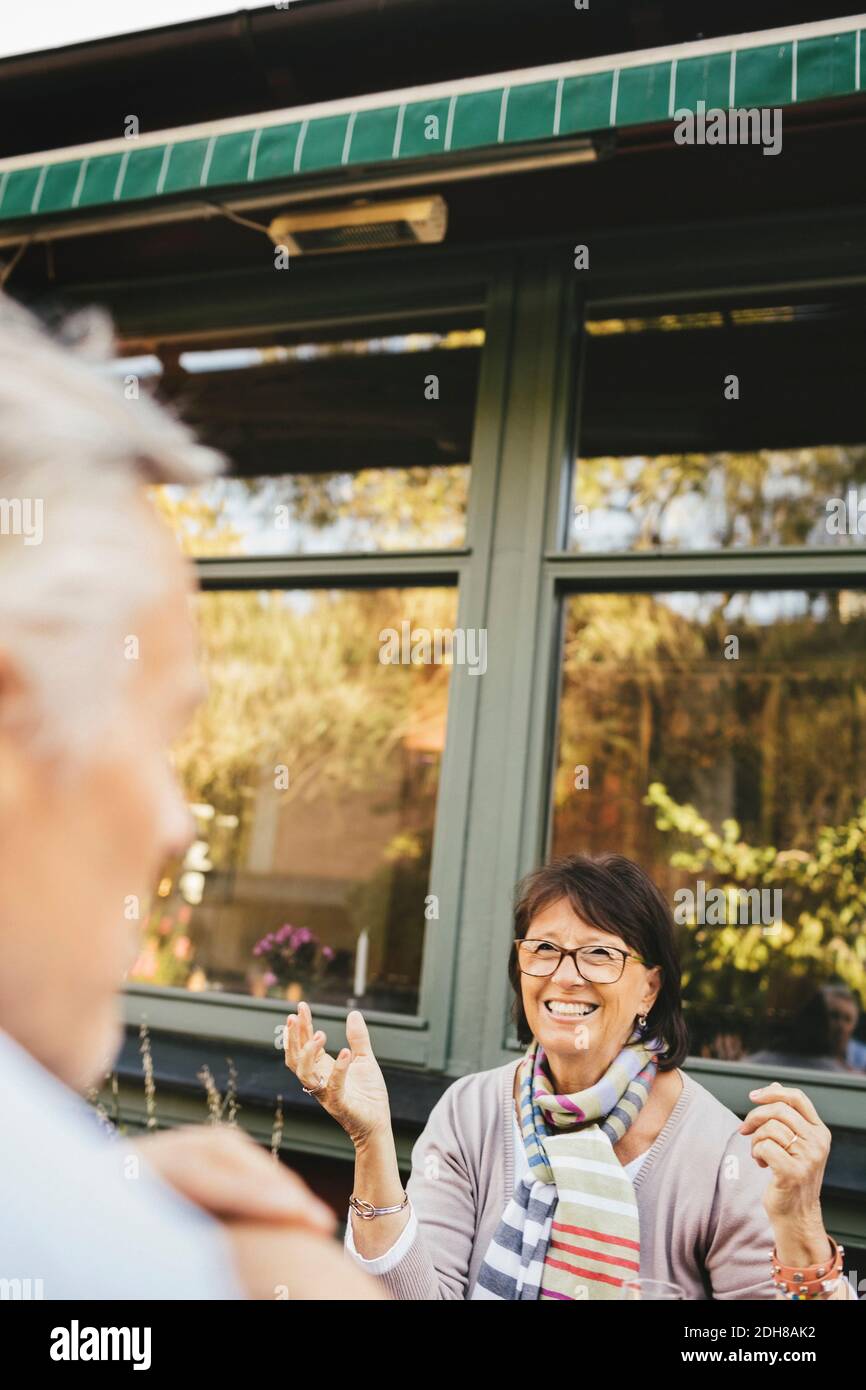 Lächelnde ältere Frau, die im Café im Freien gestikuliert Stockfoto