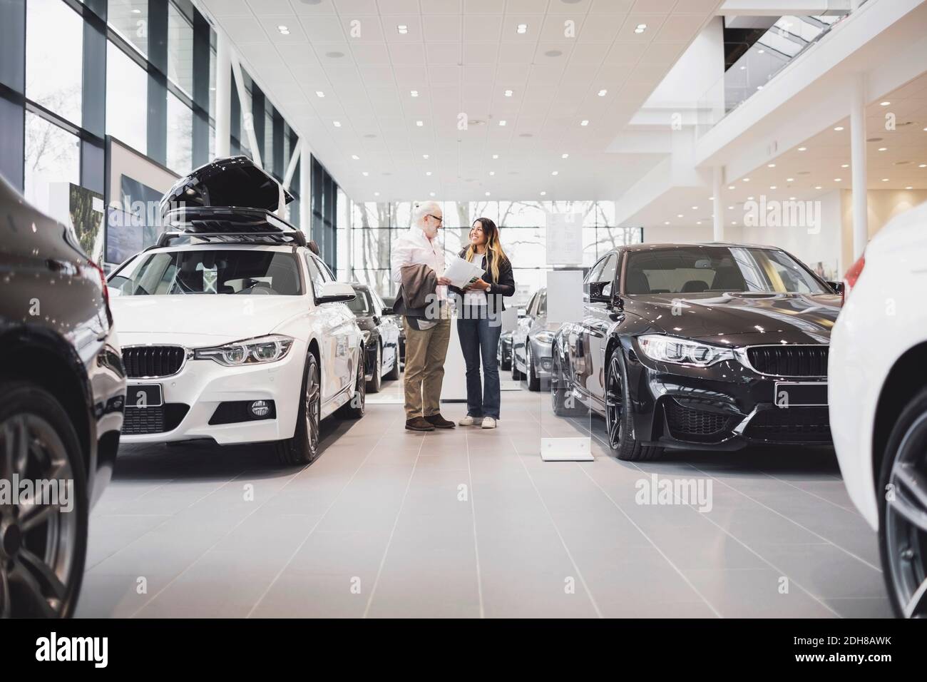 Mann und Frau mit Papier stehen inmitten von Autos im Ausstellungsraum Stockfoto