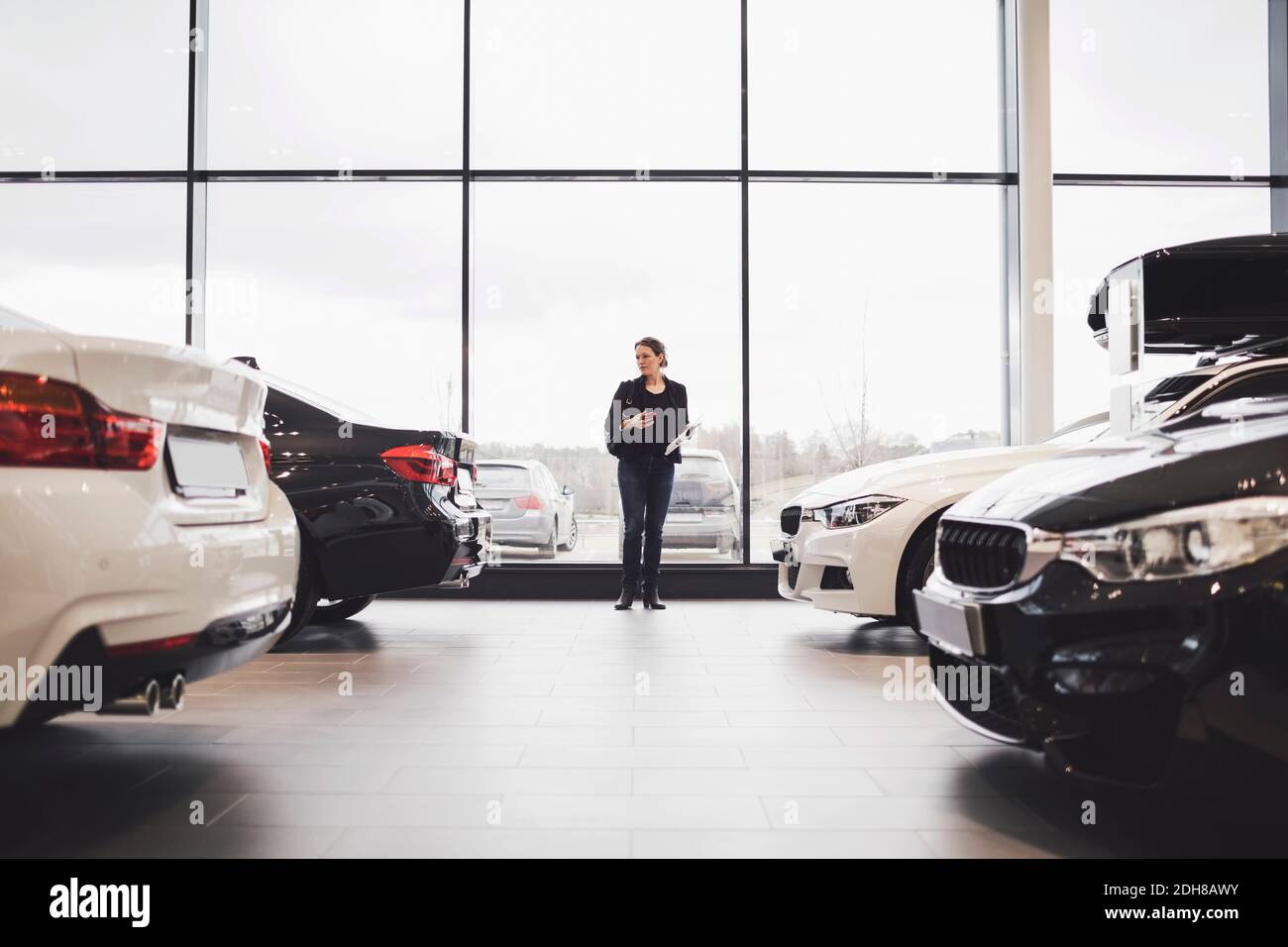 Die ganze Länge der Frau, die inmitten von Autos im Ausstellungsraum steht Stockfoto