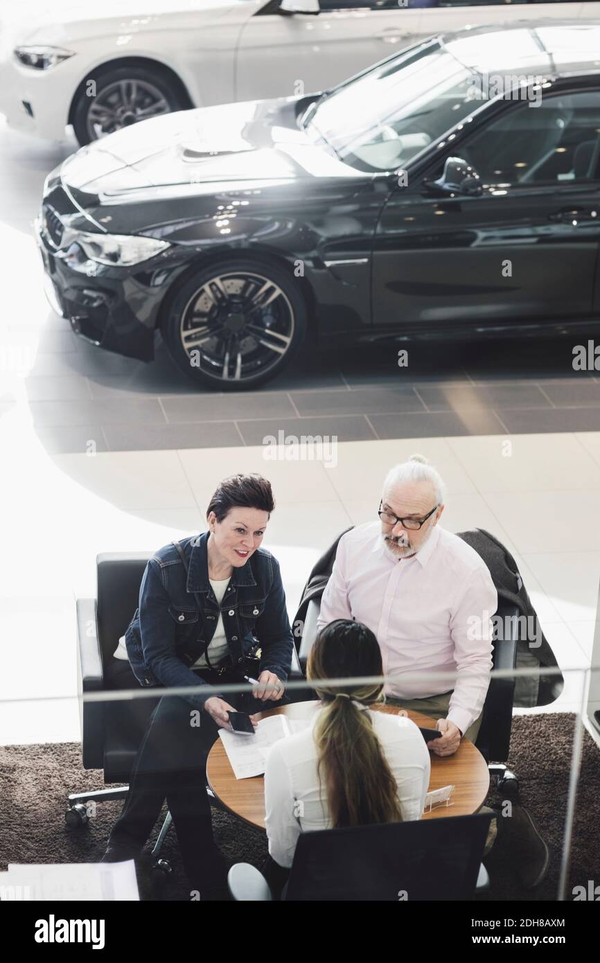 Blick auf Kunden, die mit einem Autoverkäufer Papiere unterschreiben Im Ausstellungsraum Stockfoto