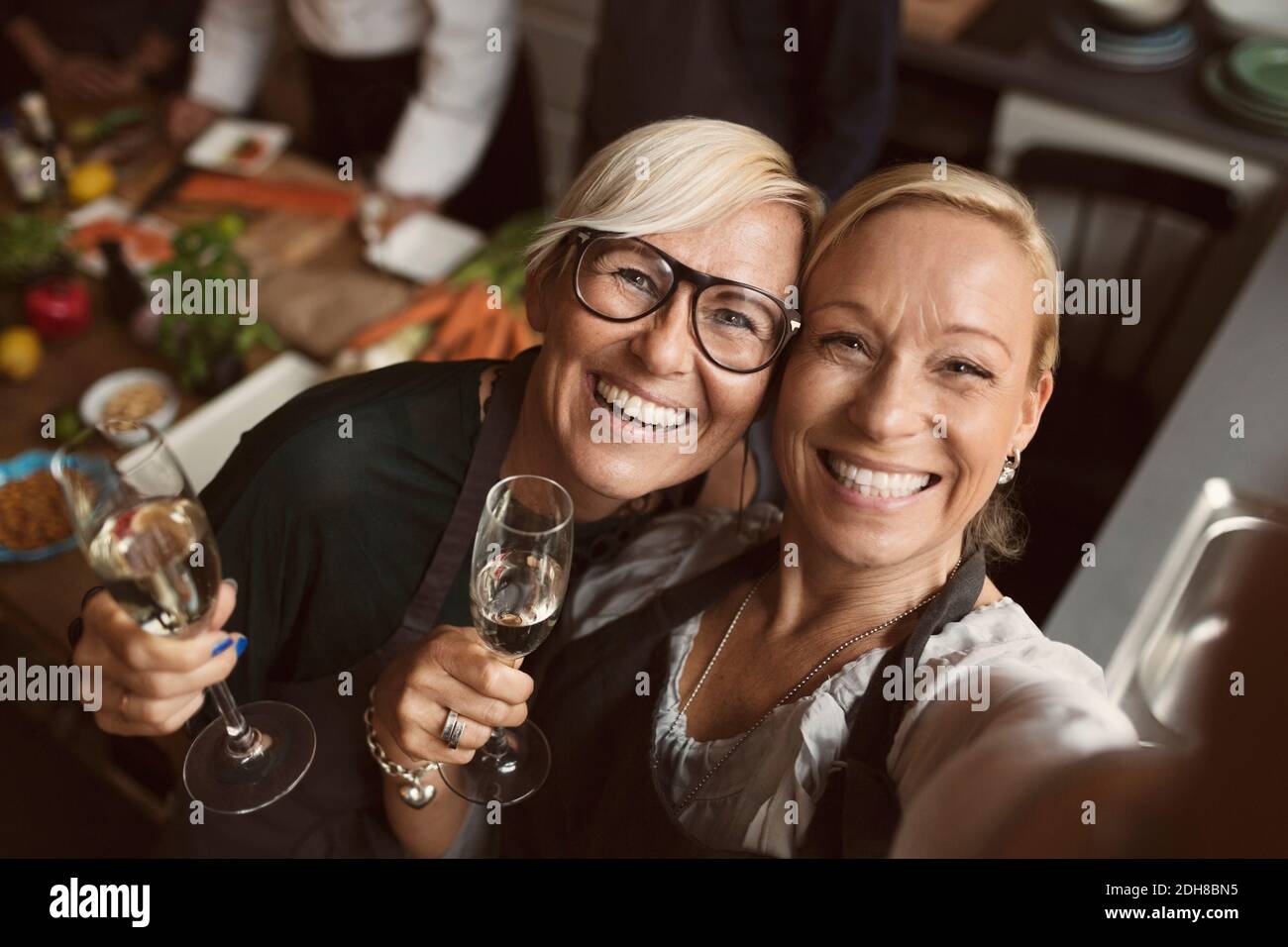 Fröhliche reife Frauen halten Champagnerflöten, während sie Selfie in Küche Stockfoto