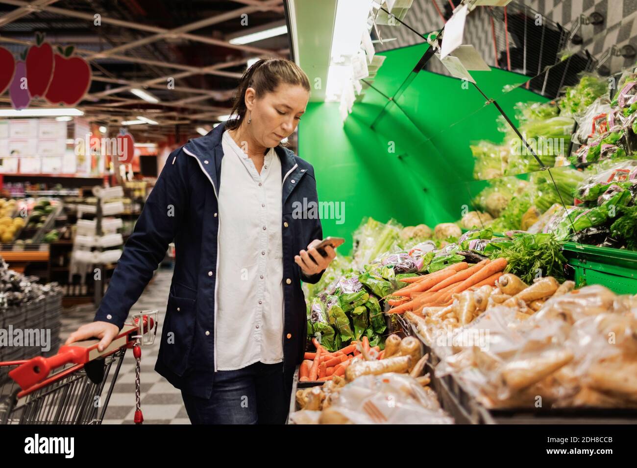 Frau mit Smartphone beim Einkauf von Lebensmitteln im Supermarkt Stockfoto
