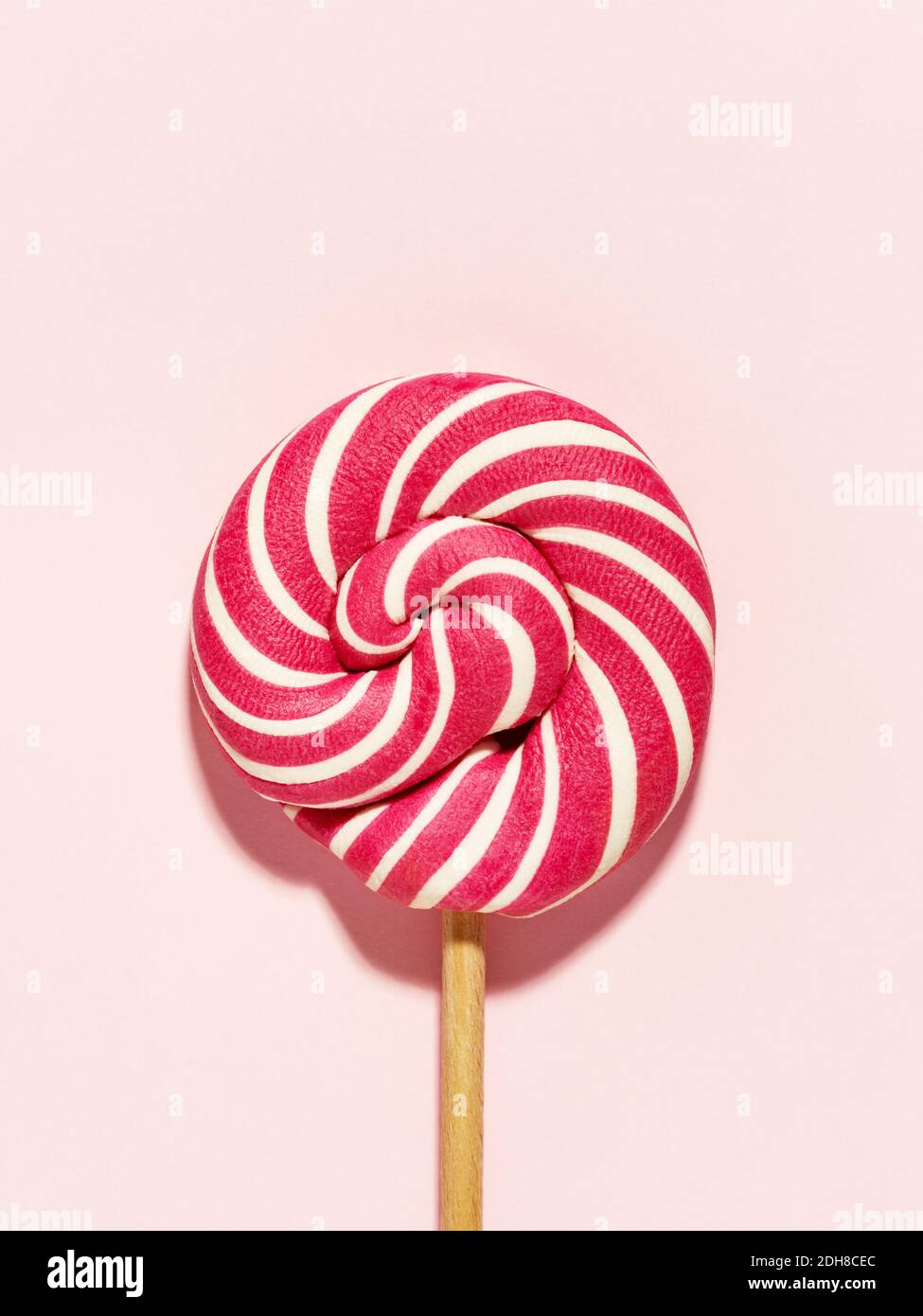 Wirbelige rote und weiße Lollipop Süßigkeiten auf rosa Hintergrund. Flach liegend, minimal. Geburtstagskonzept. Stockfoto