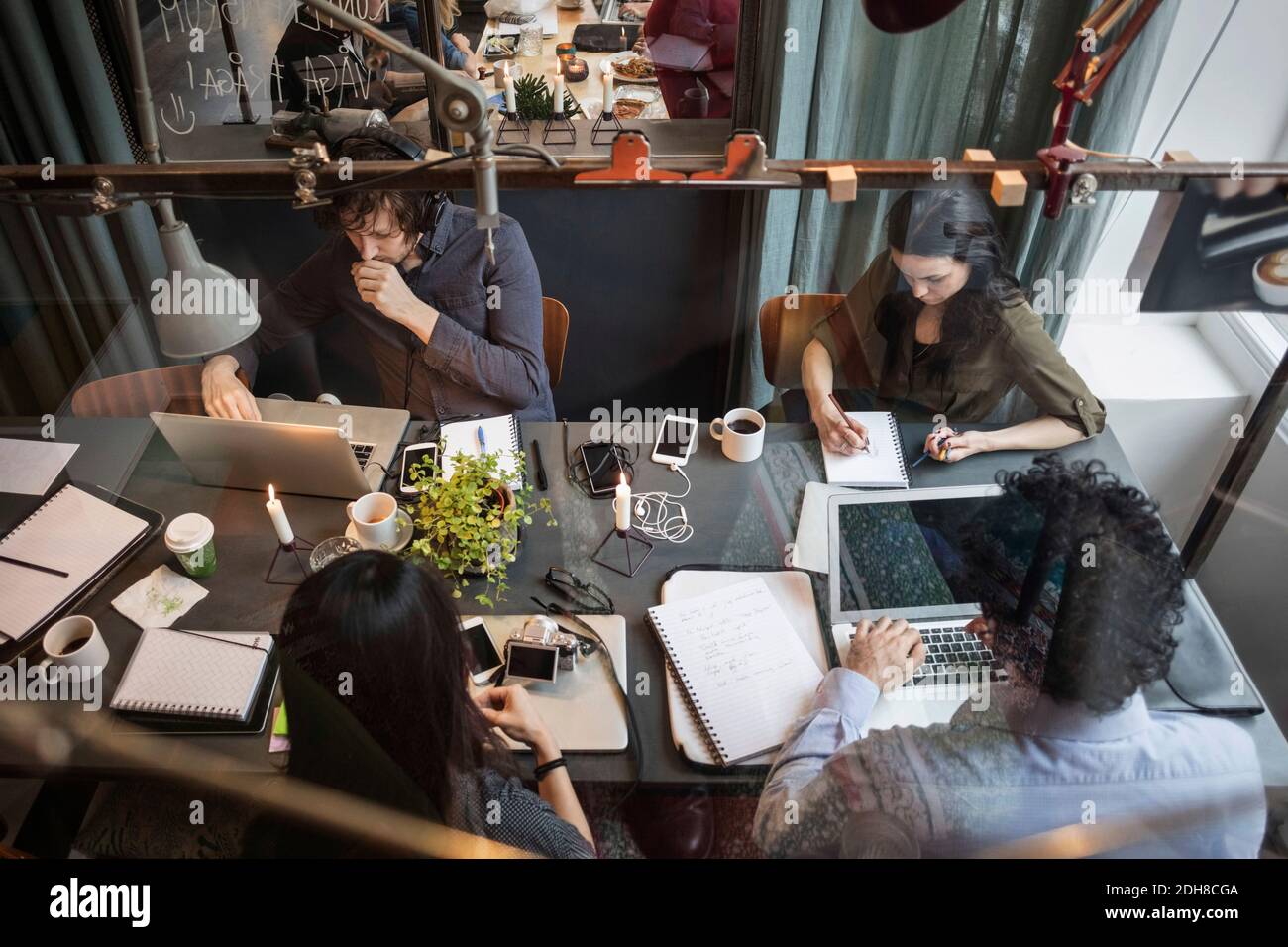 Blickfeld des kreativen Teams, das am Tisch arbeitet Büro durch Glas gesehen Stockfoto
