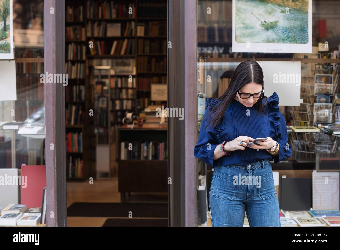 Frau, die Smartphone benutzt, während sie vor der Buchhandlung steht Stockfoto