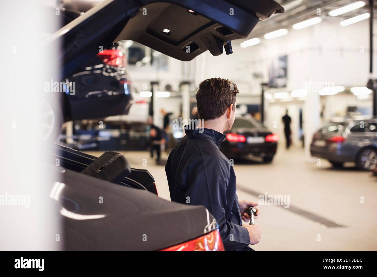 Seitenansicht des Mechanikers, der sich auf dem Kofferraum des Autos stützt Stockfoto